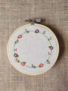 a cross - stitch hoop with flowers on it sitting on a piece of fabric next to a sewing needle