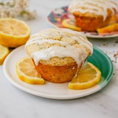 two lemon muffins with icing on a plate next to sliced lemons