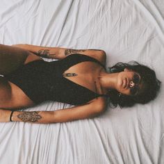 a woman laying on top of a bed in a black bathing suit and tattoos around her neck