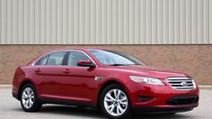 a red car is parked in front of a building with a brick wall behind it