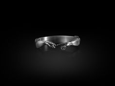 a black and white photo of a silver bracelet with two hands on the side, against a dark background