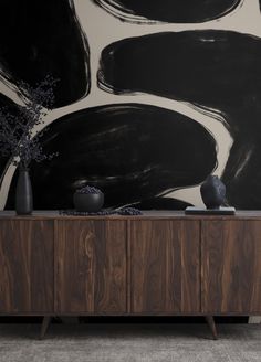 a black and white painting on the wall next to a wooden cabinet with vases