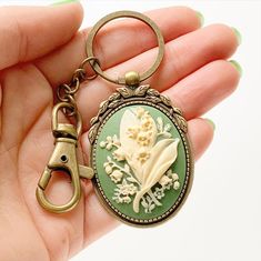 "Lily of the Valley Keychain Cameo Key Chain Floral Accessories -I make these keychains using your choice of Antique Silver or Antique Brass hardware, keychain hook along with a large clasp for clipping onto purses or adding other keychain accessories to; rose cameo is green and cream -Nickel free and lead free alloy metal, resin cameo -Select your finish from the dropdown menu -Measures 3\" long (from top of round keyring to bottom of cameo) x 1 3/8\" wide (cameo width) -Gift Boxed More of my L Keychain Hook, Bridesmaid Favors, Small Pin, Antique Brass Hardware, Cameo Brooch, Floral Accessories, Lily Of The Valley, Locket, Antique Brass