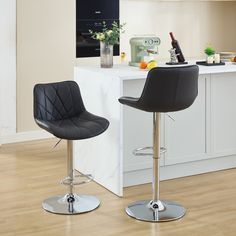 two black bar stools sitting in front of a white counter top and wooden floor