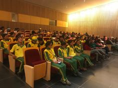 a large group of people sitting in chairs with green and yellow uniforms on their shirts