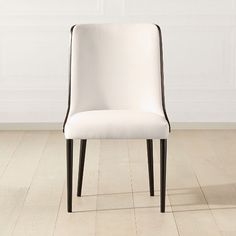 a white dining chair with black legs on a wooden floor in front of a white wall