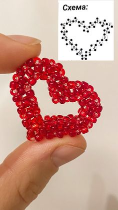 a hand holding a piece of red glass beaded heart brooch with the word cxema on it