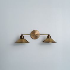 two lights are on the wall in front of a white wall and one light is gold