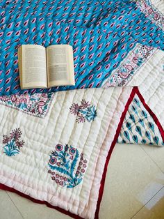 an open book laying on top of a blue and white quilted blanket with red trim