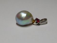 This is 18kt white gold white with strong bluish grey rose overtones in color Cultured ? Pearl and Natural Ruby Corundum gemstone pendant with medium size bail. The very fine quality transparent in Clarity, Red Color Excellent Faceted Round Cut Ruby gemstone measures and weighs approximate 3.0 mm weighing .10 points carat total weight. The Cultured ? Pearl has white with strong gray bluish rose overtone's in color, measure 1/3 inch x 1/2 inch in Size, natural oblong shape, excellent luster, moderate naturally blemished surface quality and acceptable nacre. It appears to have some type of glue at top of pearl attached to pendant. This very old pendant has a bail stamped 750 and in very good condition. Condition of this fine quality Ruby and Cultured Pearl pendant is excellent and weight 2.2 White Gold Gemstone Pendant For Formal Occasions, Elegant Silver Pear-shaped Gemstones, Pear-shaped Platinum Jewelry As Gift, Silver Drop Jewelry With High Luster, White Gold Drop Jewelry With High Luster, White Gold Drop Earrings With High Luster, High Luster Silver Drop Jewelry, High Luster White Gold Drop Jewelry, Platinum Drop Jewelry Gift