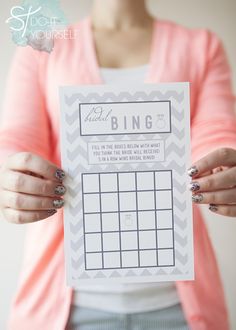 a woman holding up a printable photo to show off her bridal bingo game