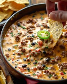 a hand dipping a tortilla chip into a bowl of chili and cheese dip