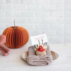 two folded napkins on a plate next to an ornament and a pumpkin