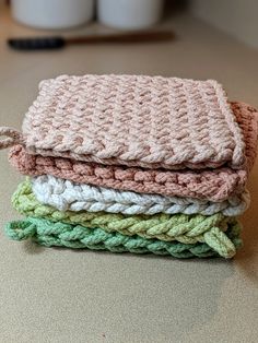 four knitted blankets stacked on top of each other in different colors and sizes, sitting on a table