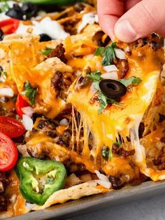 a person taking a slice of nachos from a pan with peppers, onions and cheese