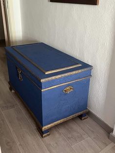 a blue chest sitting on top of a hard wood floor next to a white wall