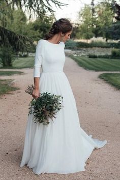 a woman in a long white dress holding a bouquet and looking down at the ground