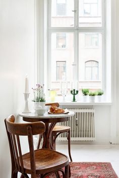 two chairs and a table in front of a window with a red rug on the floor