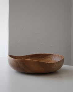 a wooden bowl sitting on top of a white table next to a wall and window