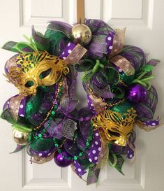 a purple and green mesh wreath with gold masks on the front door for mardi gras