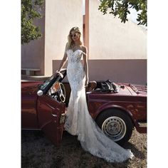 a woman in a wedding dress standing next to a red car with the door open