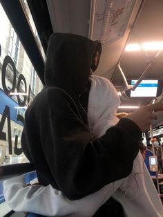 a person wearing a hoodie on a bus looking at their cell phone while holding something in his hand