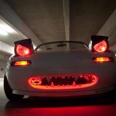 a white sports car parked in a parking garage with its lights on and the hood up