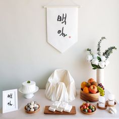 a white table topped with plates and bowls filled with fruit next to a wall hanging