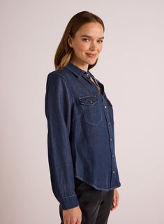 This long sleeve shirt features a classic western style in a dark denim wash, perfect for pairing with denim on denim or faux leather pants. Made from soft Tencel blend fabric, this versatile shirt can be worn open with a cami or tank underneath for a stylish look. This shirt is a timeless addition to any wardrobe, offering both comfort and style. 54% TENCEL™ lyocell 24% Linen 22% Viscose. SIZE CHEST SHOULDER TO HEM XS 19" 18 7/8" S 20" 19 1/2" M 21" 20 1/8" L 22" 21 1/4" Classic Denim Top With Snap Buttons, Classic Fitted Denim Top With Pockets, Classic Long Sleeve Denim Top, Indigo Shirt For Workwear In Fall, Denim Blue Button-up Top For Rodeo, Denim Blue Long Sleeve Shirt For Rodeo, Long Sleeve Denim Blue Shirt For Rodeo, Classic Dark Wash Denim Top With Snap Buttons, Classic Dark Wash Denim Top With Button Closure