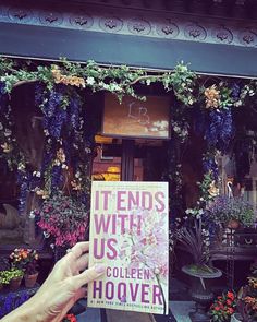 someone holding up a book in front of a flower shop