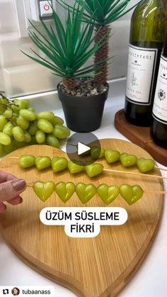 a wooden cutting board topped with green grapes next to bottles of wine and a potted plant