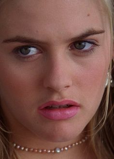 a close up of a woman with blue eyes and pearls around her neck looking at the camera