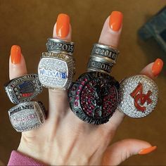 a woman's hand with five rings on it, including an orange nail polish