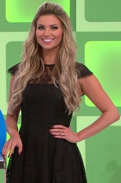 a woman standing in front of a green wall wearing a black dress and holding her hands on her hips