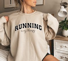 "Embrace the therapeutic rhythm of the run with our \"Running Is My Therapy\" sweatshirt! ot just for the track or trail, this sweatshirt is versatile. Throw it on after a run, or make it your comfy go-to for chilly days. Running is a lifestyle, and now your wardrobe reflects it. HOW TO ORDER: 1. Choose size/color options 2. Select the quantity 3. Click \"Add to Cart\" 4. Proceed to payment Sweatshirt Features: - Premium blend Organic Cotton  - Relaxed fit/ Unisex - Available in sizes S - 5XL Care Instructions: To keep your sweatshirt looking its best, follow these care instructions: - Machine wash cold with like colors. - Use only non-chlorine bleach when needed. - Tumble dry low or hang to dry for best results. - Iron on low heat if necessary, avoiding the printed area. SIZING: While the Sporty Fleece Sweatshirt For Gym, Sporty Sweat-resistant Running Hoodie, Sportswear Hoodie For Running And Sports Season, Athletic Heather Long Sleeve Sweatshirt For Gym, Sporty Workout Sweatshirt Hoodie, Sporty Workout Hoodie Sweatshirt, Athleisure Hoodie For Running During Sports Season, Athleisure Hoodie Sweatshirt For Sports Events, Athleisure Running Hoodie For Sports Season