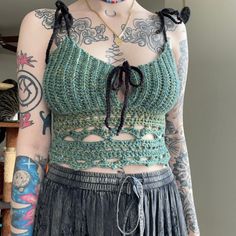 a woman with tattoos on her body wearing a green crop top and black pleated skirt