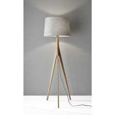 a wooden tripod floor lamp with a white shade on the top, and a light grey wall behind it