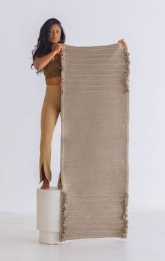 a woman standing on top of a white pedestal holding up a tan rug with fringes