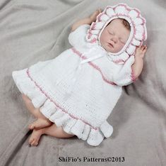 a baby is wearing a white crochet dress and bonnet while laying on a bed