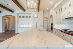 a large kitchen with white cabinets and marble counter tops, along with a chandelier hanging from the ceiling