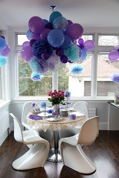 the table is surrounded by many different colors of balloons and paper flowers on top of it