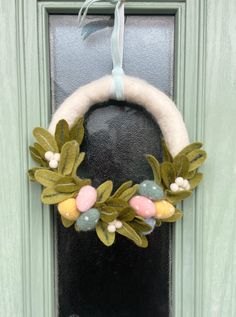 a wreath hanging on the front door of a green house with flowers and leaves painted on it