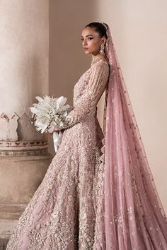 a woman in a pink gown and veil standing next to a pillar with flowers on it