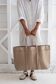 a person holding two bags in their hands and standing next to a white wall with shelves behind them