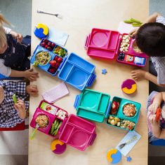 several children are sitting at a table eating lunches and playing with their hands on the trays