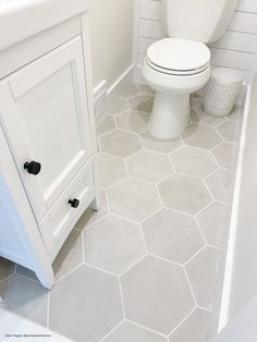 a white toilet sitting in a bathroom next to a sink and shower stall with hexagonal tiles on the floor