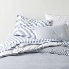 an unmade bed with blue and white striped sheets, pillows and pillowcases