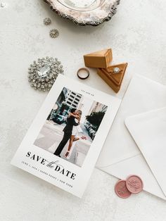 save the date cards and wedding rings on top of a white table with envelopes