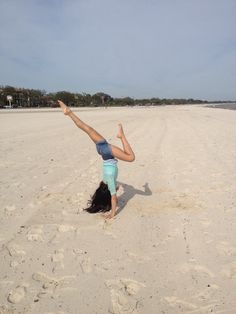 a woman doing a handstand on the beach