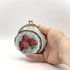 a hand holding a small purse with red roses on the front and sides, in white background